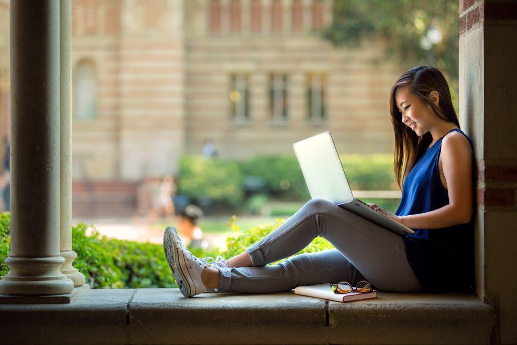 collge student sitting with her legs out and working on her laptop