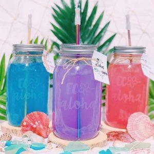 three mason jars with colorful blue purple and red liquid sitting in front of a tropical background of seashells and palm fronds.