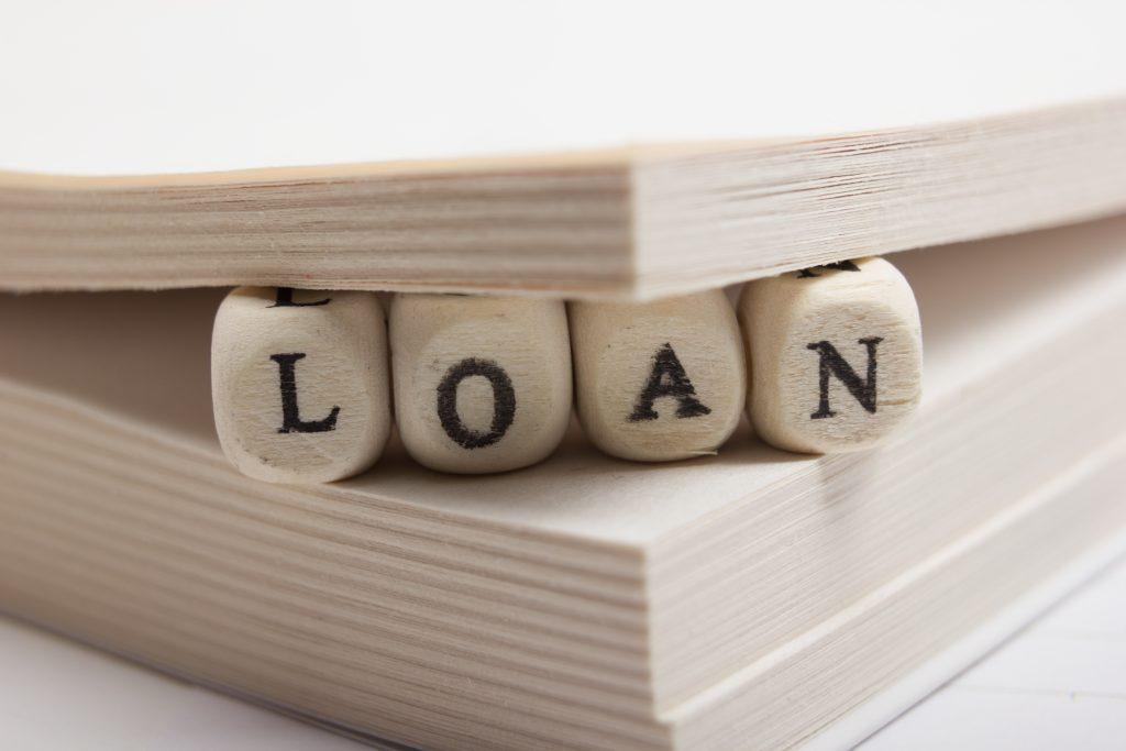 wooden blocks spell out the word LOAN between the pages of a book