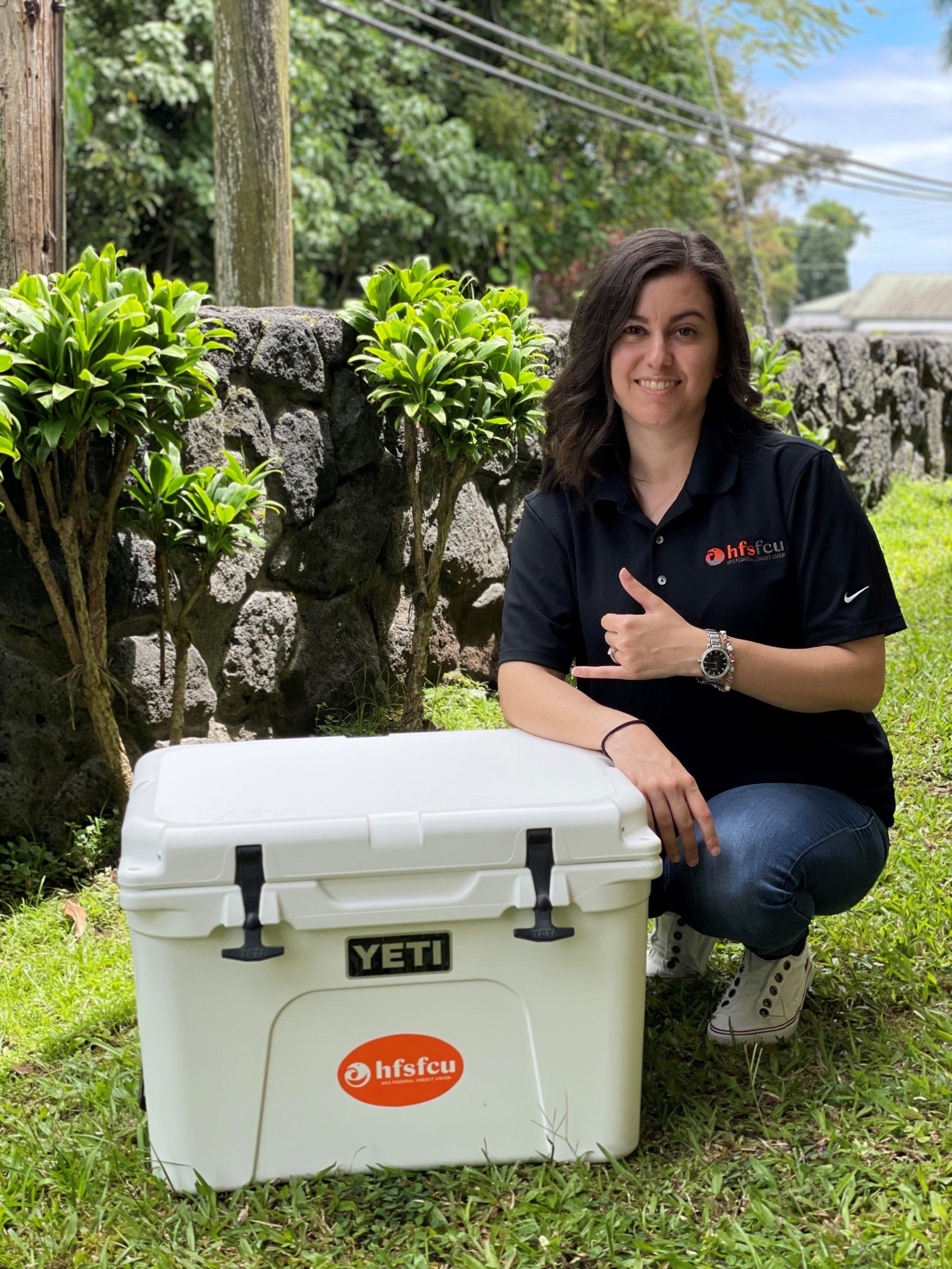 HFS Employee kneeling next to a white Yeti Cooler with an orange HFS sticker on the front